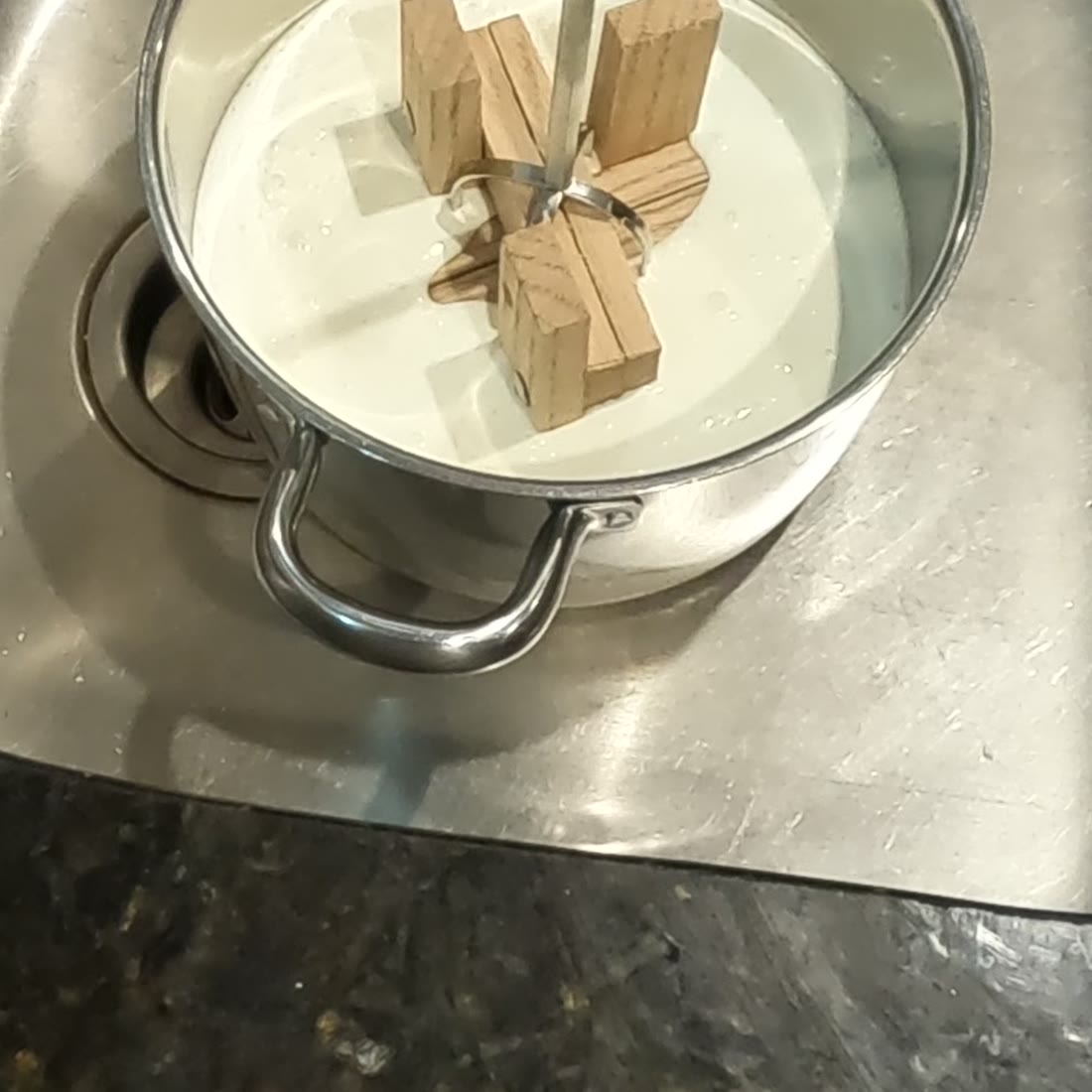 A four armed wooden churn head resting in a pot of white yogurt.