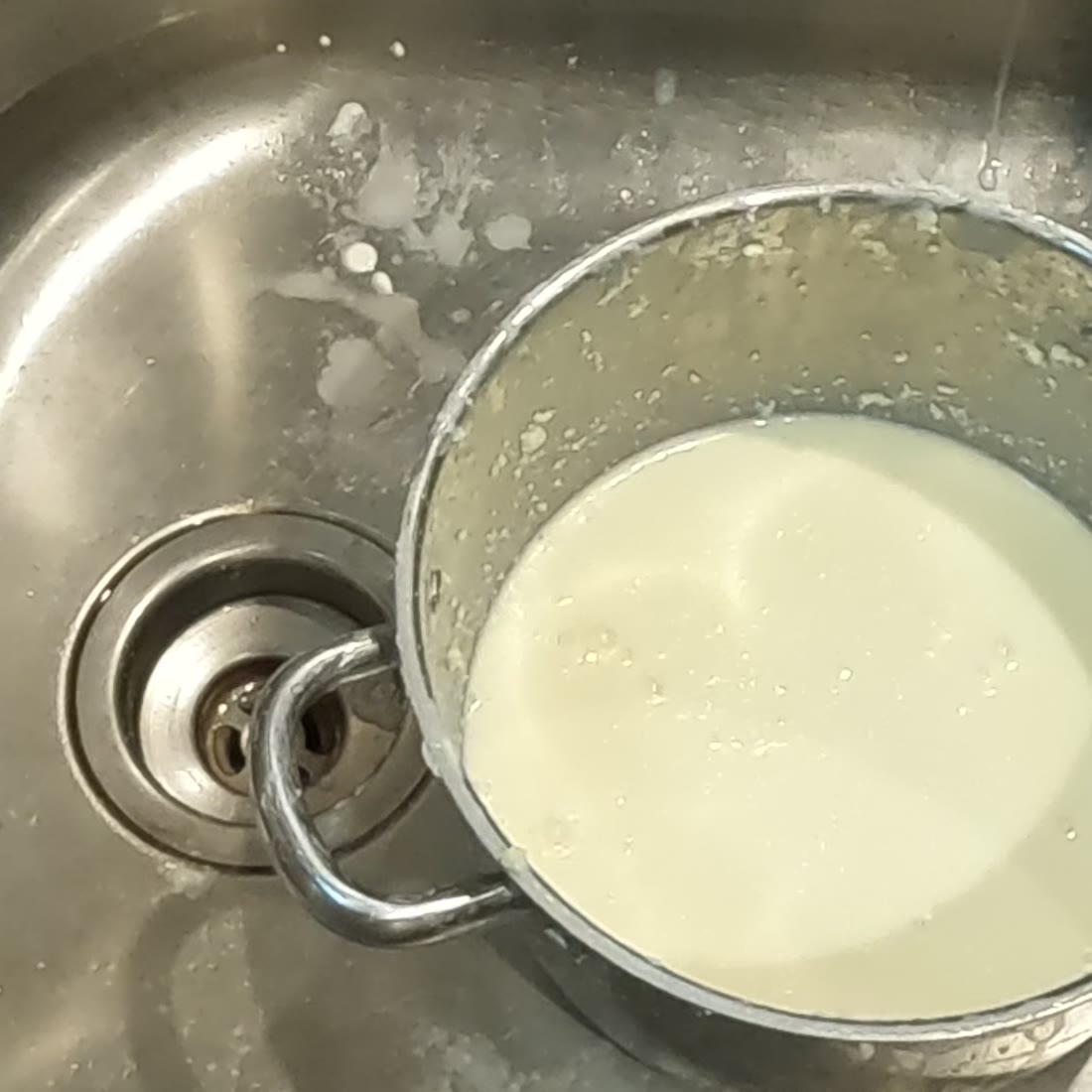 A pot of thin white buttermilk left in the sink after the butter has been lifted out.