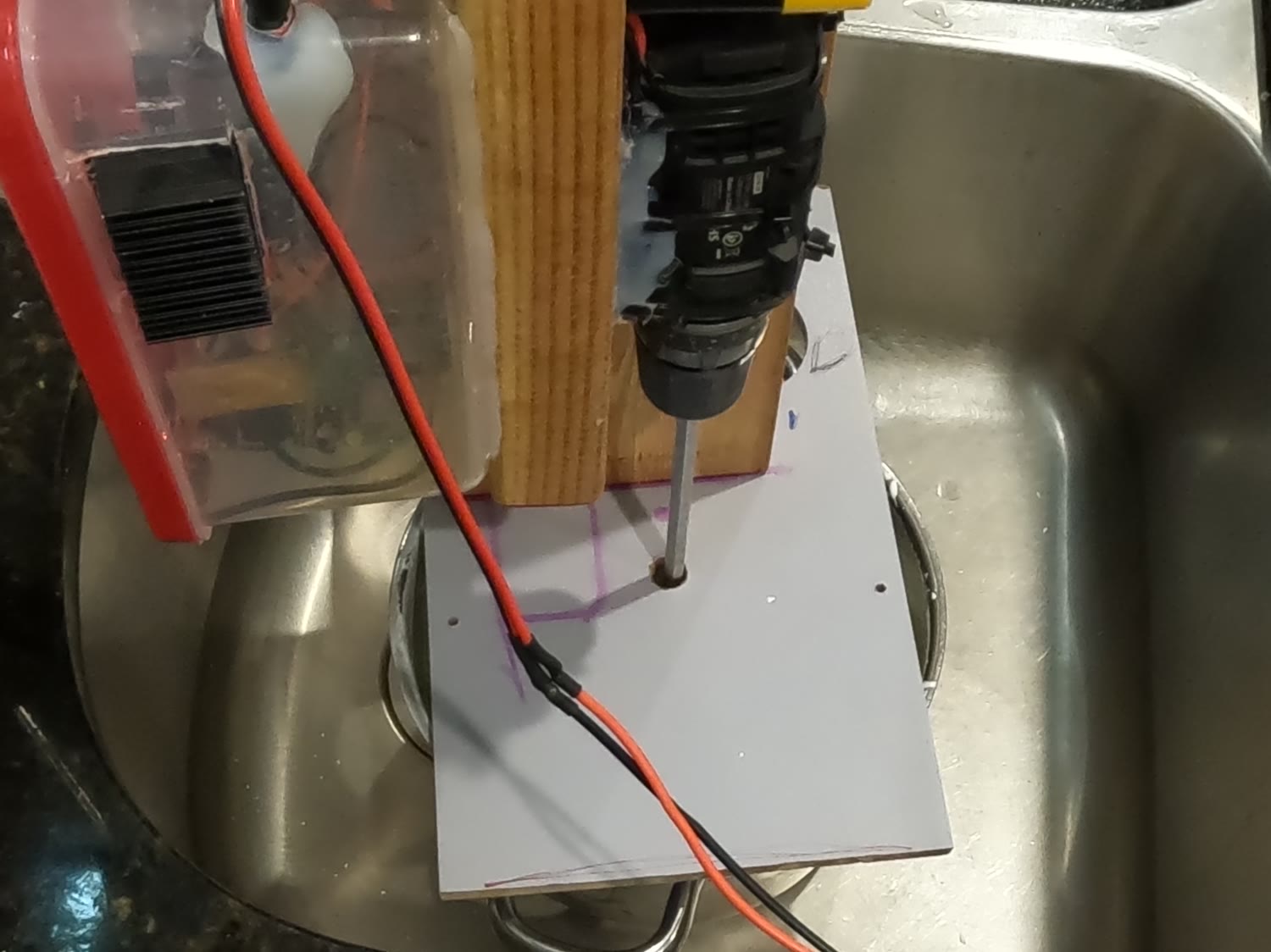 The drill running above a covered pot inside a stainless steel kitchen sink, with the electronics box alongside.