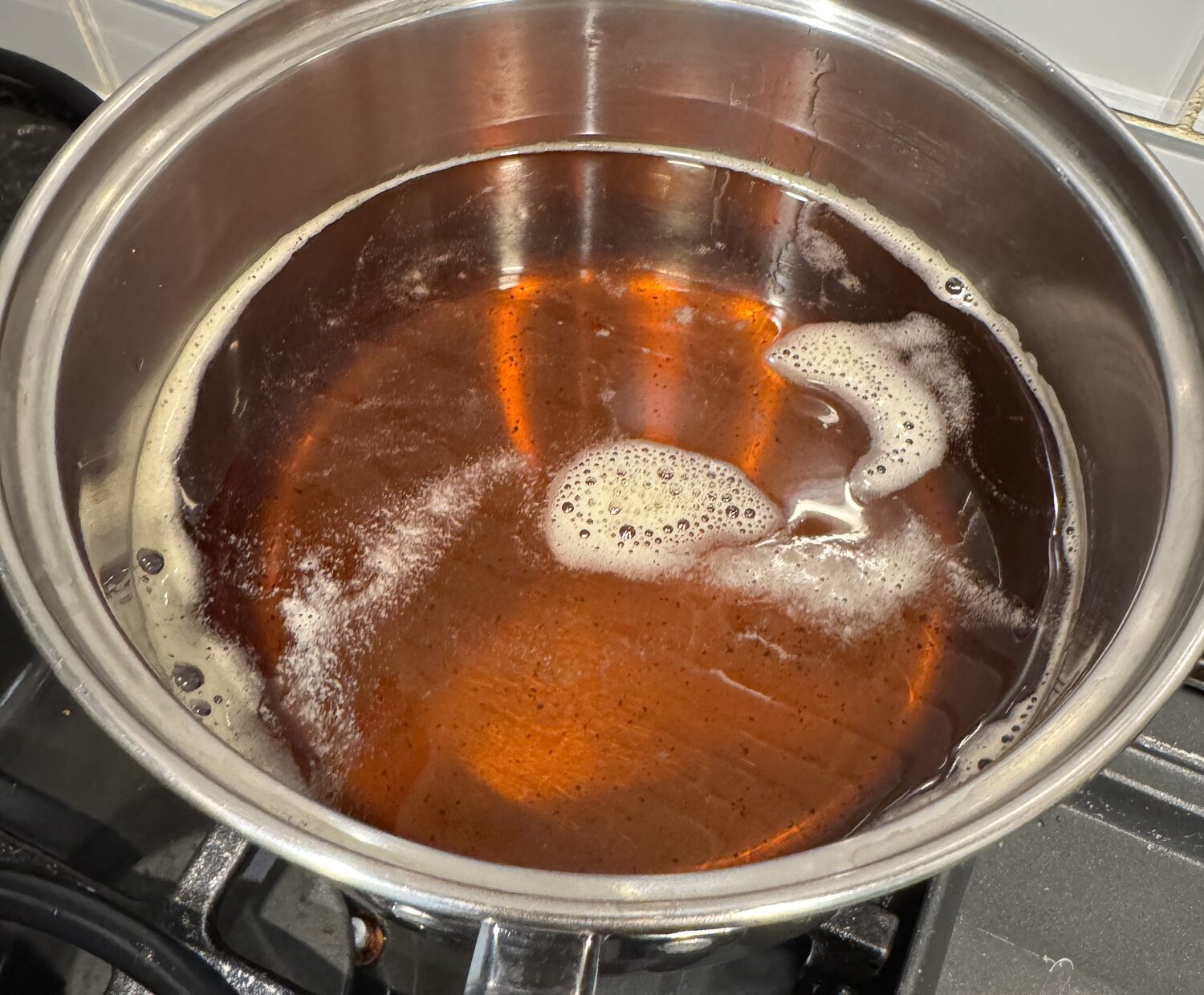 A pot of finished ghee, deep clear amber with a little foam at one edge.
