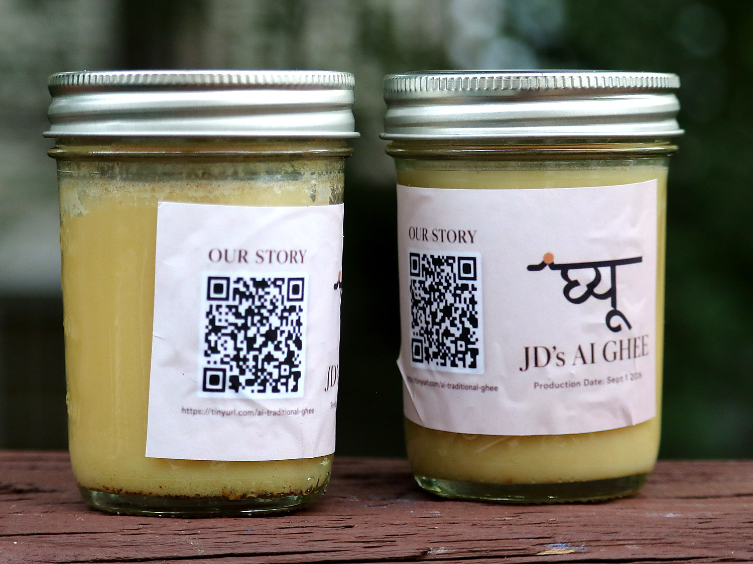 Two jars of pale set ghee on a wooden rail outdoors, each with a paper label carrying the Nepali word for ghee, the name JD's AI Ghee and a QR code.