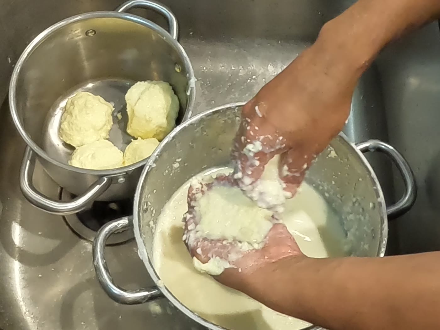 Two hands pressing loose butter curds together into a ball over a colander.