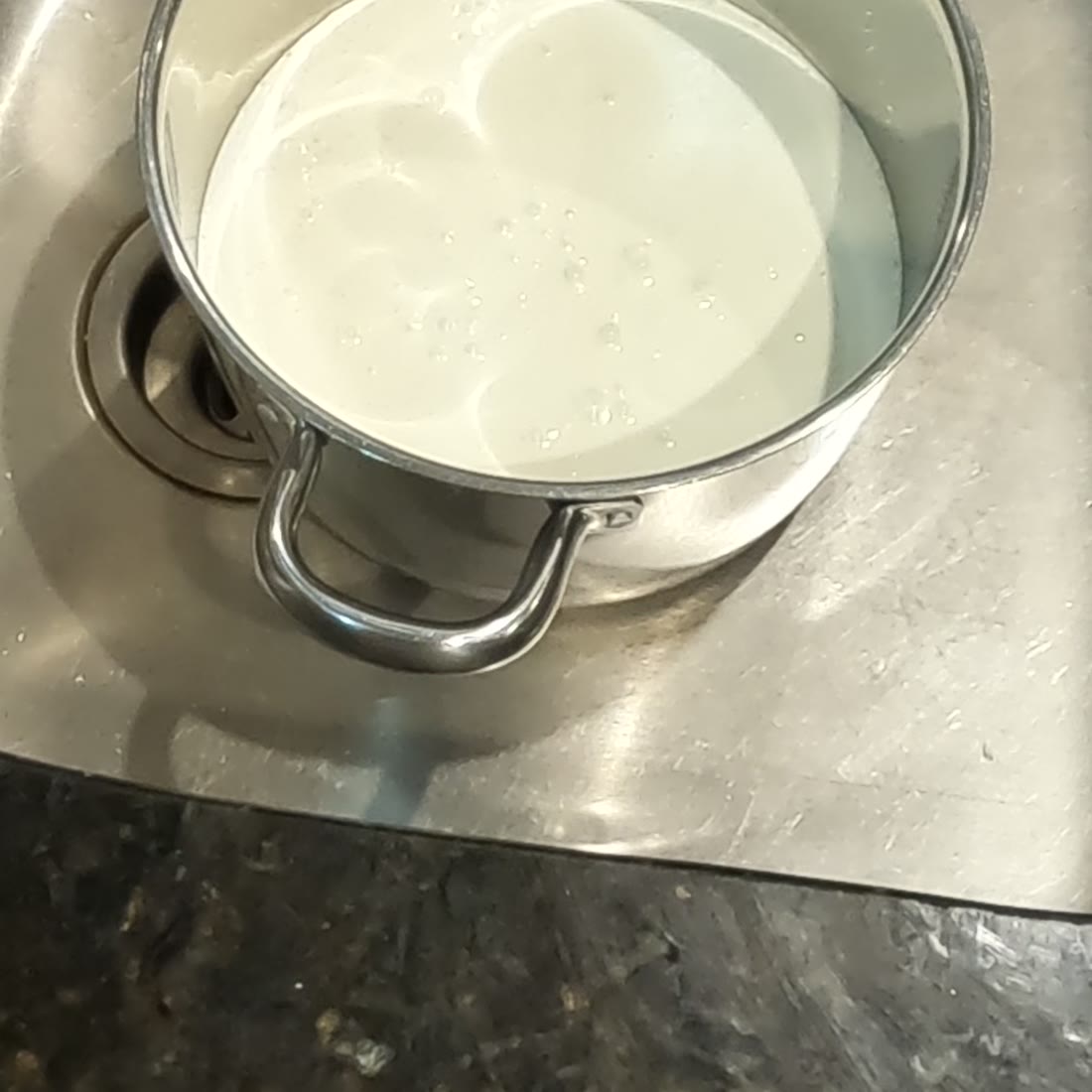 A pot of thick set yogurt sitting in a kitchen sink, ready to be churned.